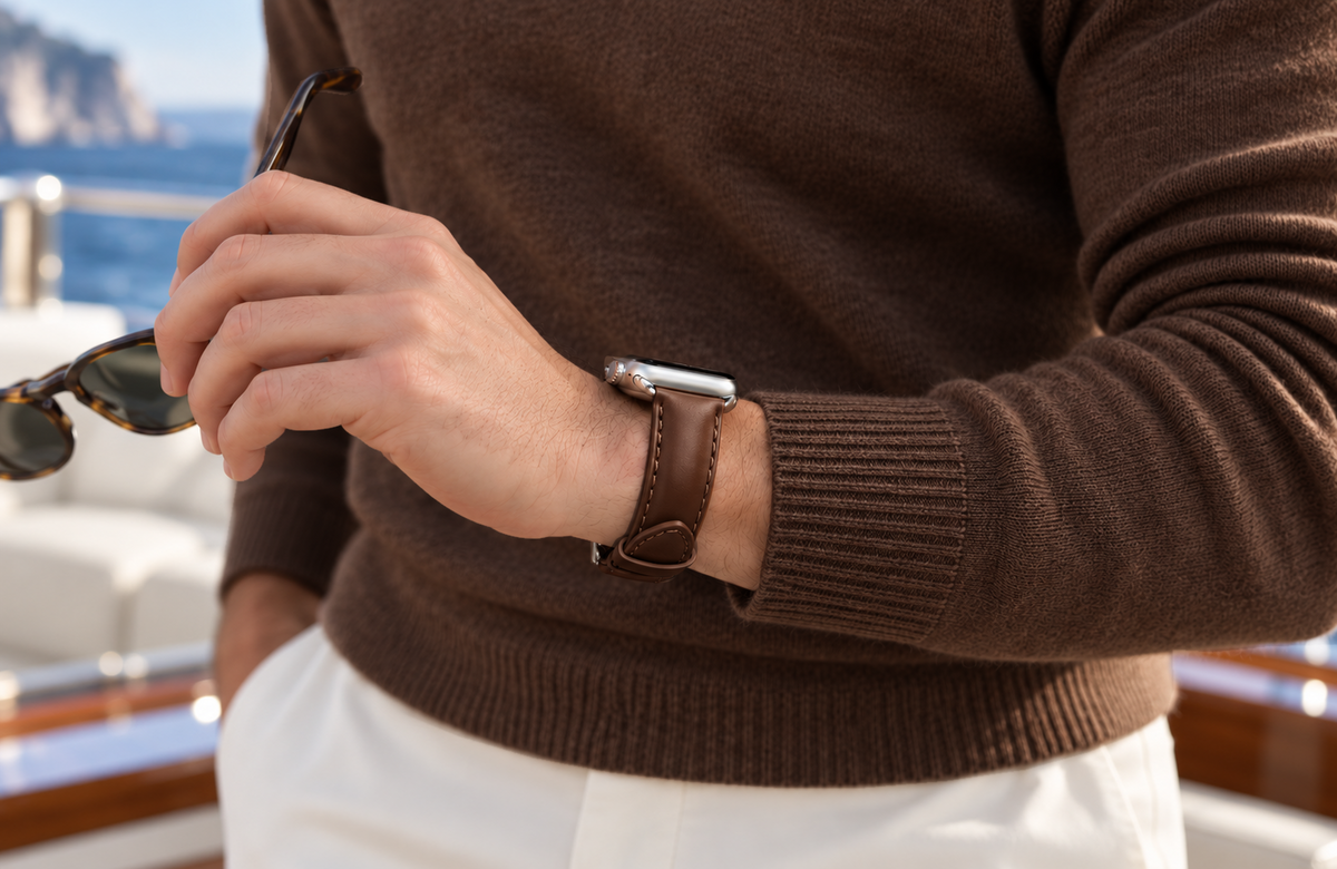 Man in a dark brown jumper holding sunglasses aboard a yacht, wearing a padded WsC Defiant dark brown leather Apple Watch strap with standard non-diamond silver hardware.