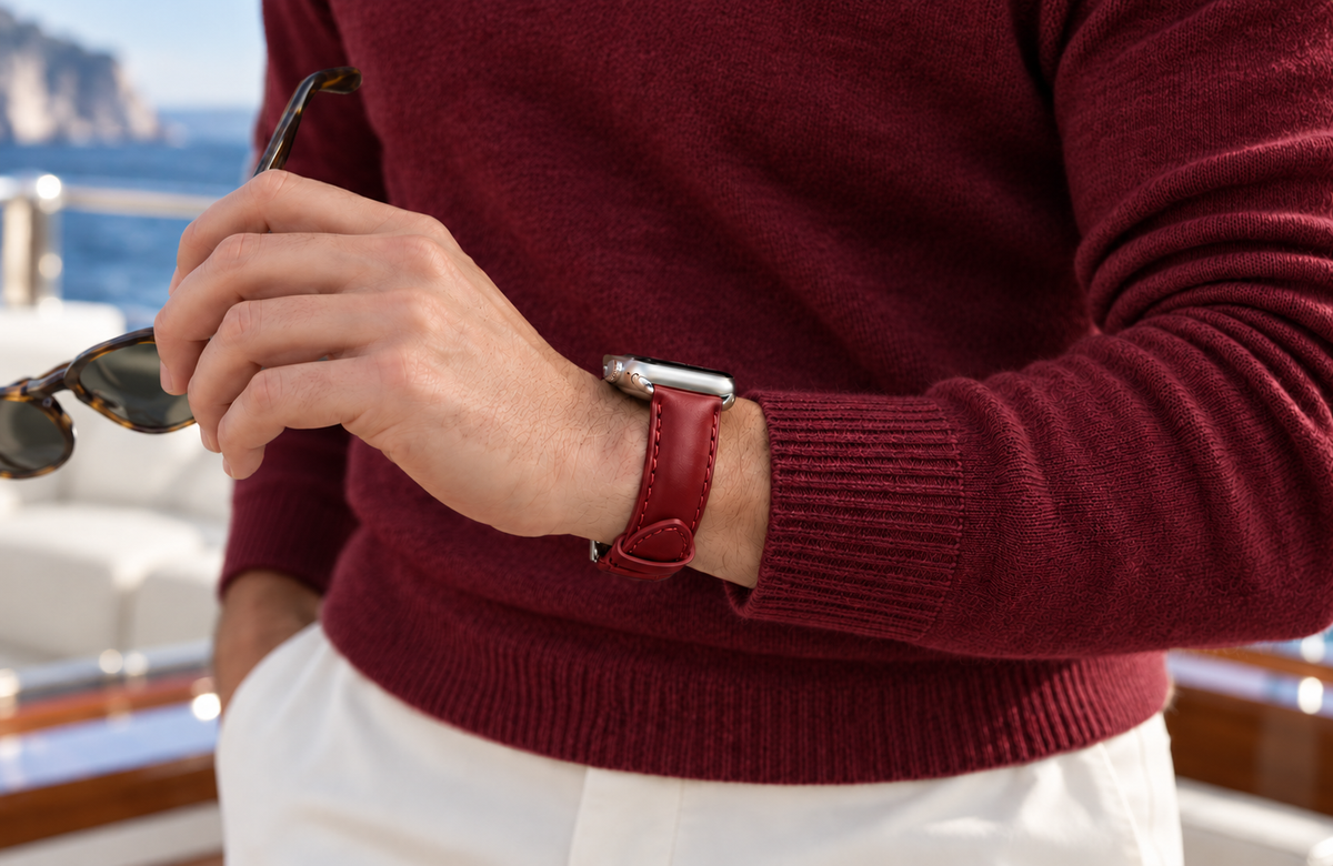 Man in a burgundy jumper holding sunglasses aboard a yacht, wearing a padded WsC Defiant red leather Apple Watch strap with standard non-diamond silver hardware.